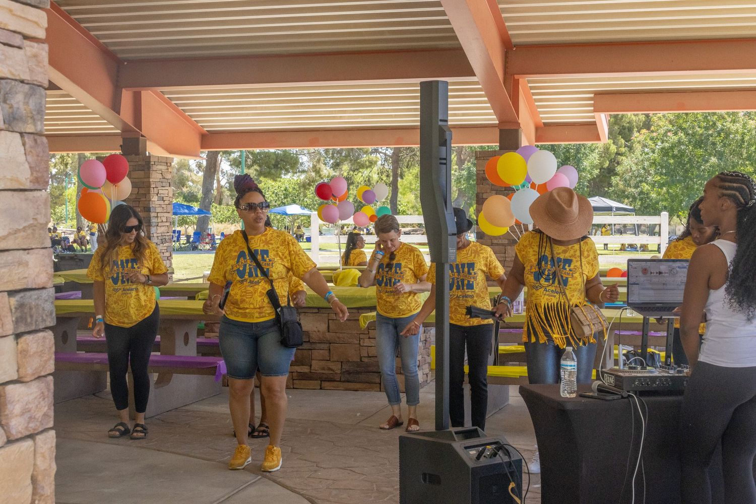 Team building activity with participants in yellow shirts dancing in formation under covered patio.