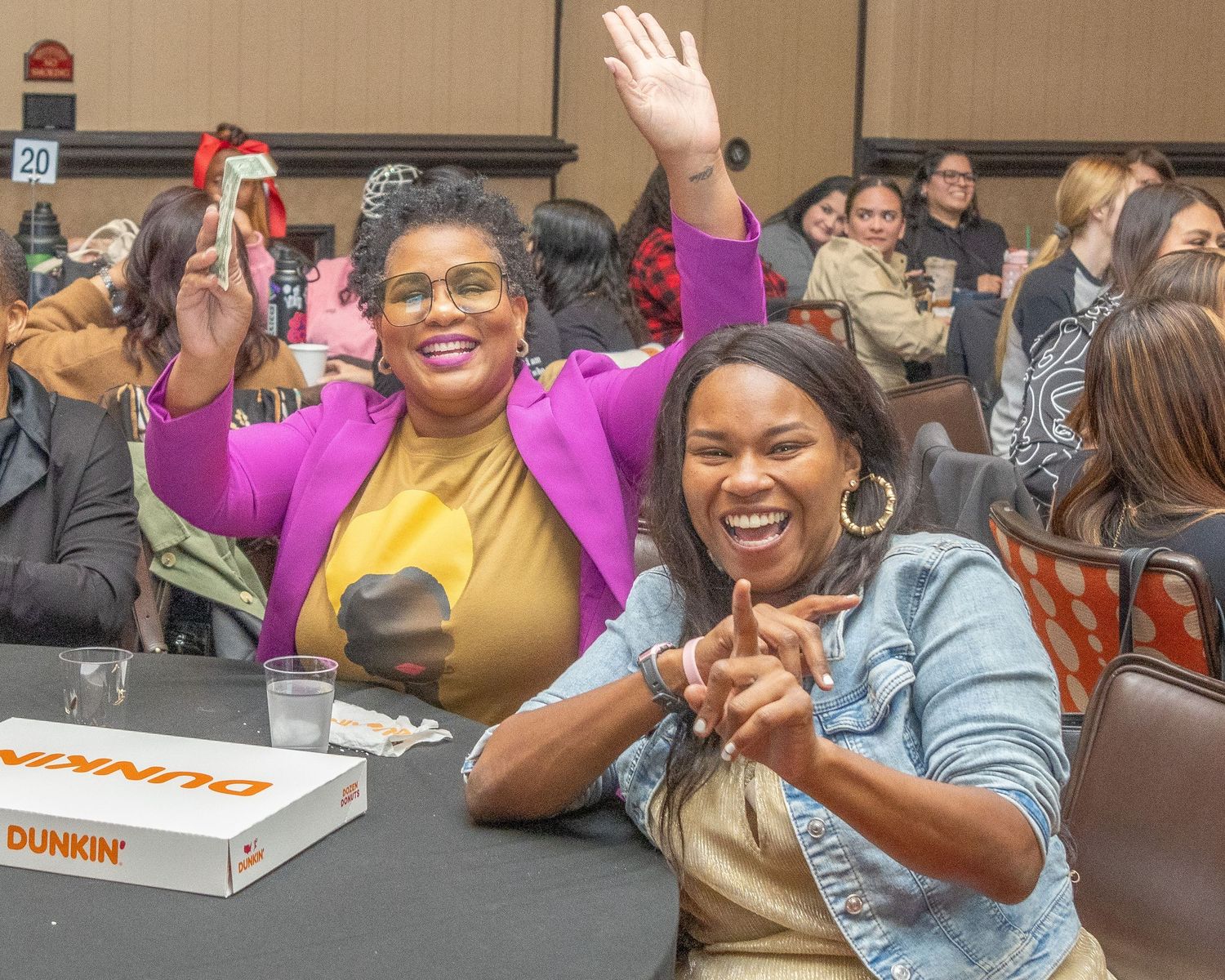 Enthusiastic attendees celebrate and laugh together with Dunkin Donuts box visible on table.