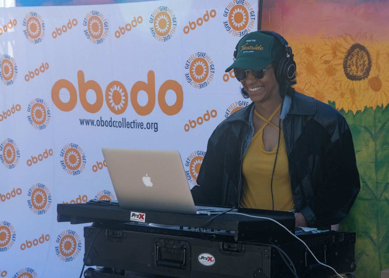 DJ performs at an event with colorful orange-branded backdrop and professional equipment setup.