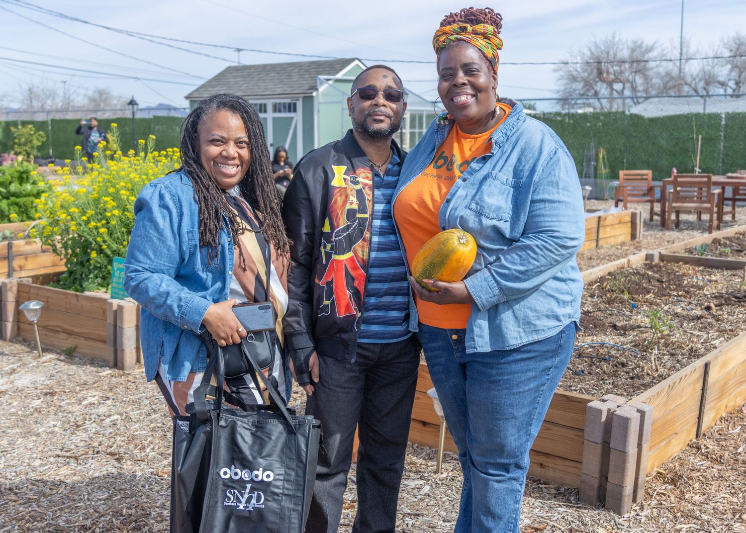 Community members work together at an urban garden with raised wooden planting beds on a spring day.