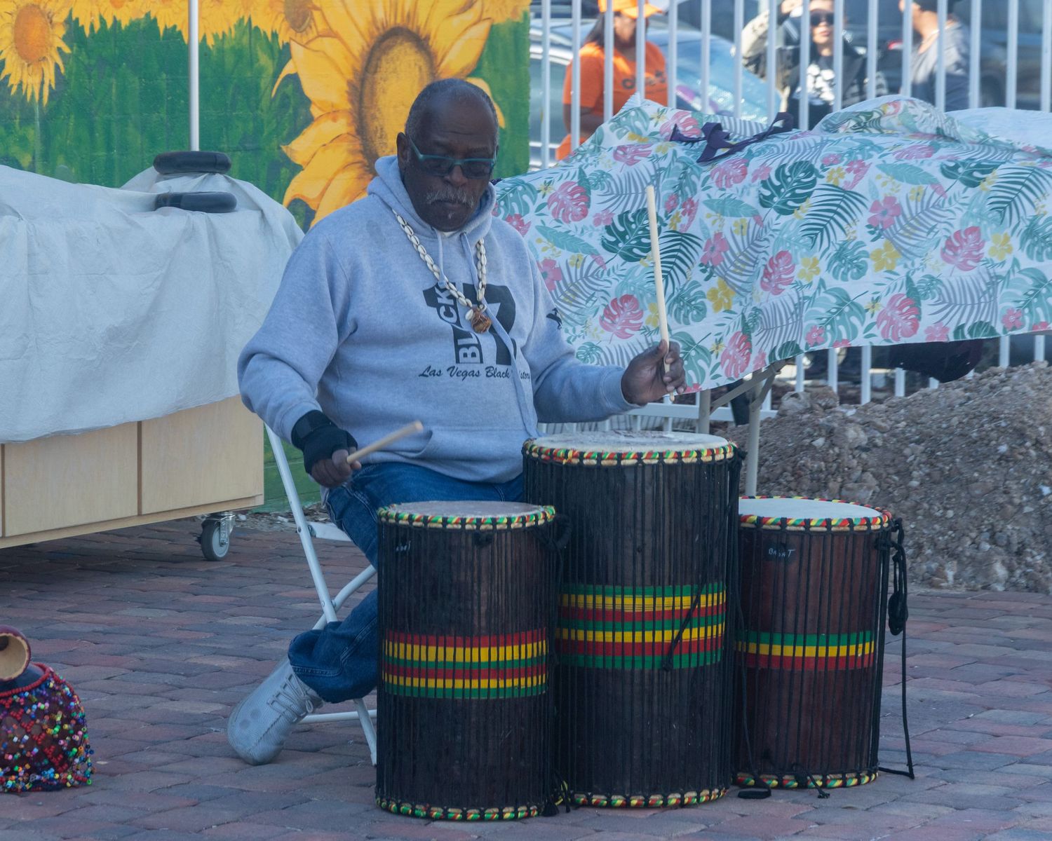 African djembe drums line up against a vibrant painted mural backdrop during a cultural performance event.