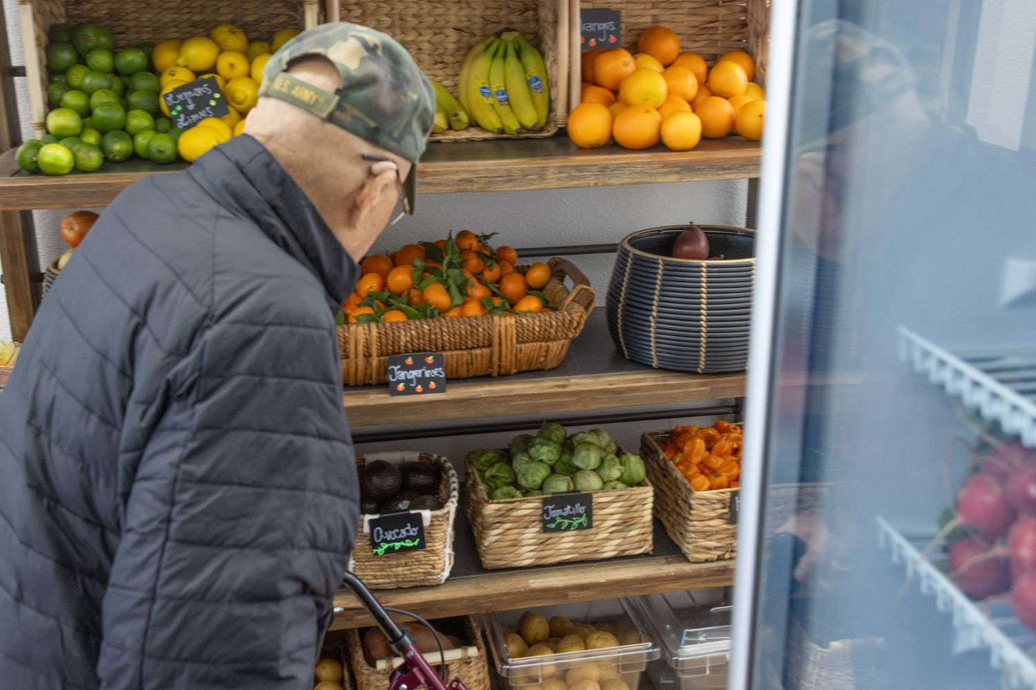 Shopper in puffy winter jacket browsing produce section with citrus fruits and apples at grocery store.