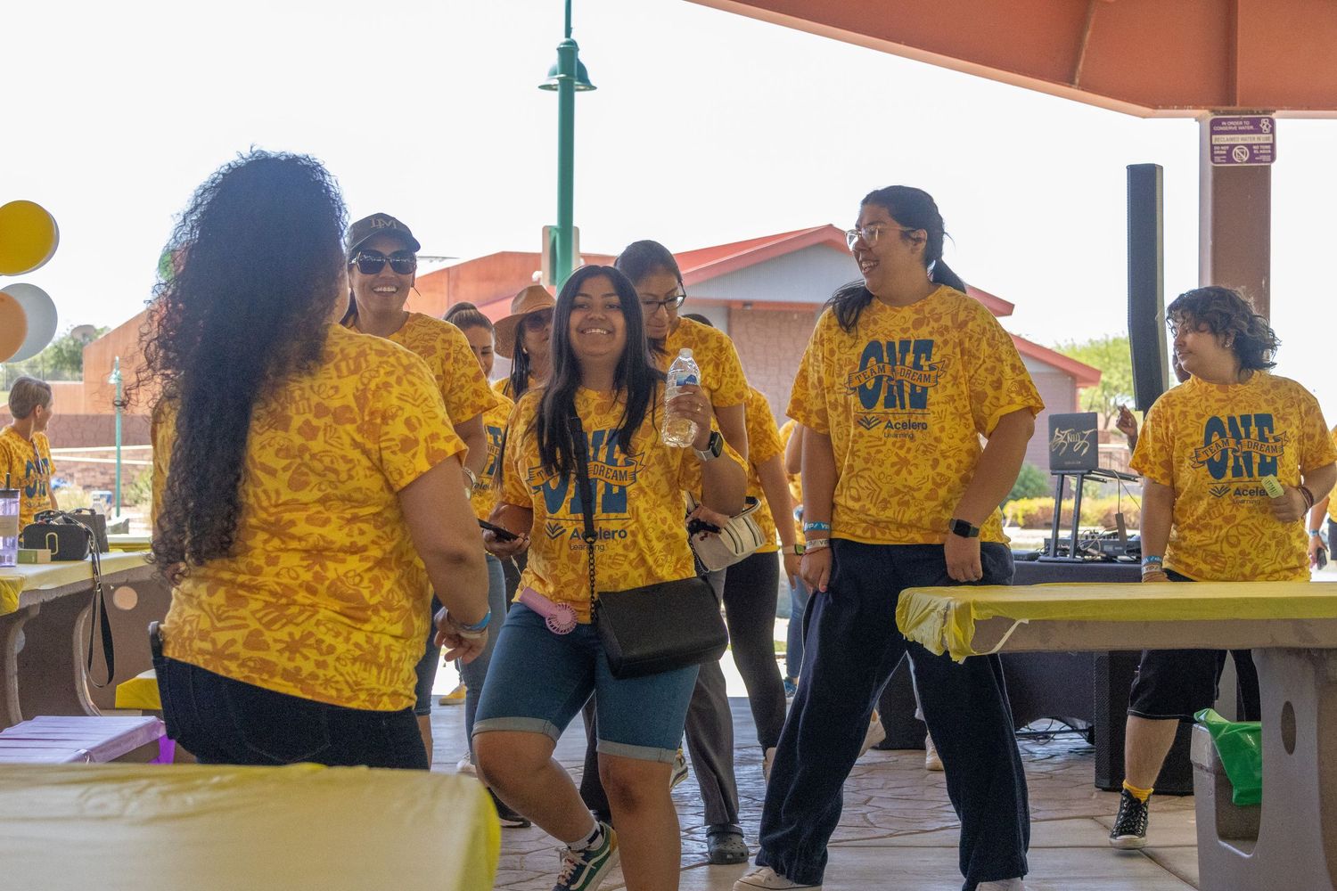 People wearing bright yellow shirts participating in a group dance activity under a pavilion.