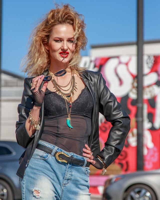 Edgy fashion look with denim overalls, leather jacket, and statement accessories against urban graffiti backdrop.