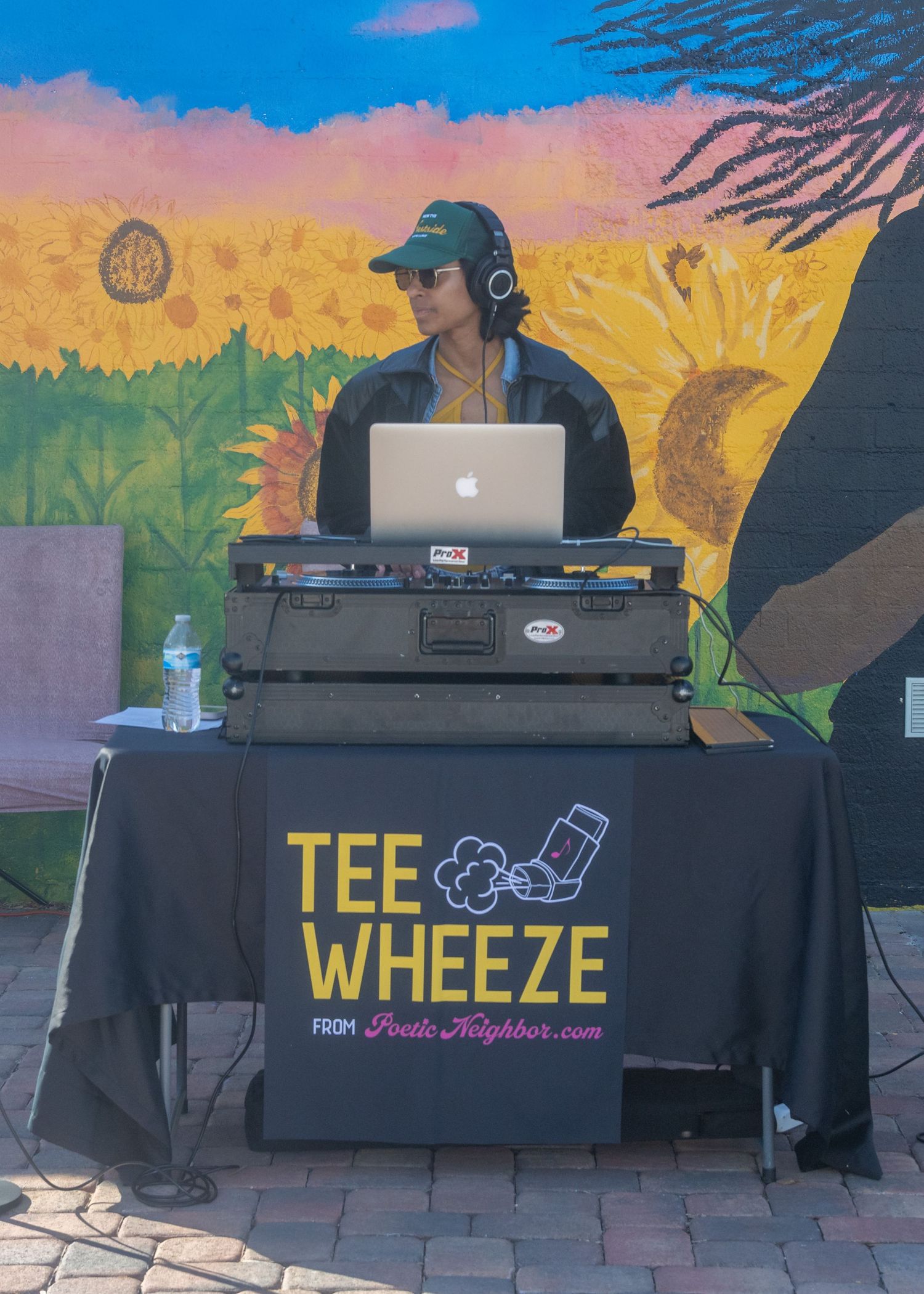 DJ equipment setup with colorful mural backdrop featuring vibrant sunset colors and landscape artwork.