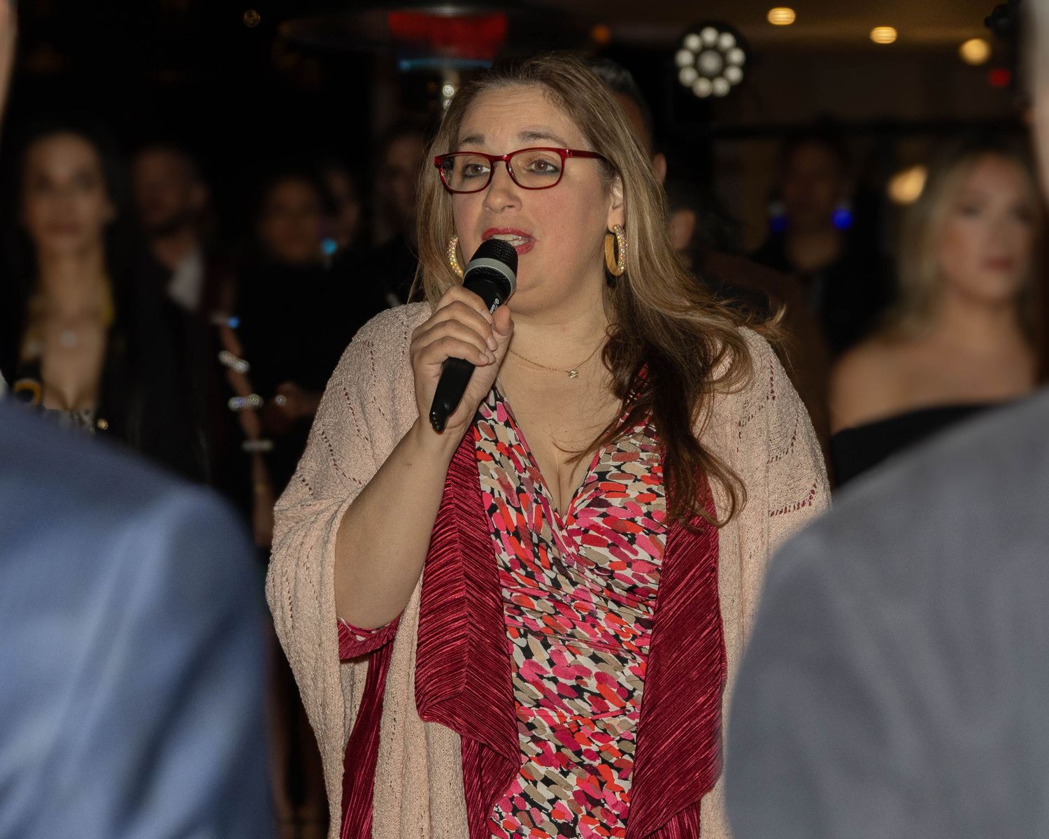 Woman in red floral dress and beige cardigan smiling at social event.