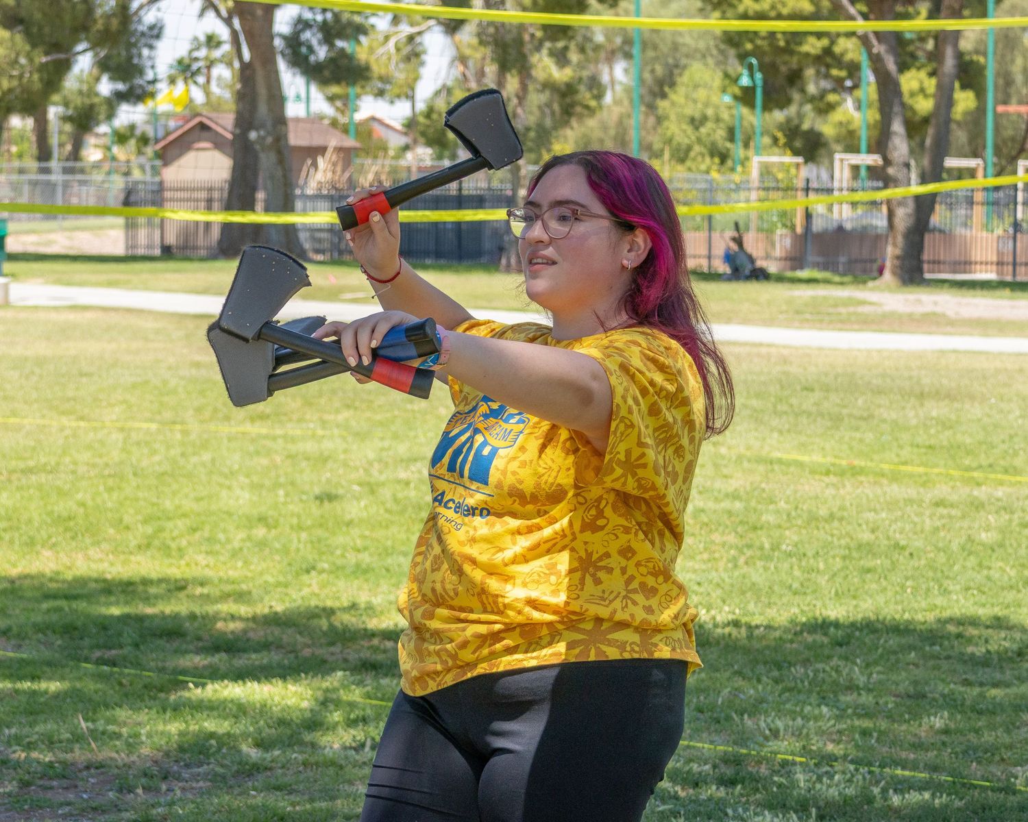 Person in yellow shirt playing ball game on grass field at community event.