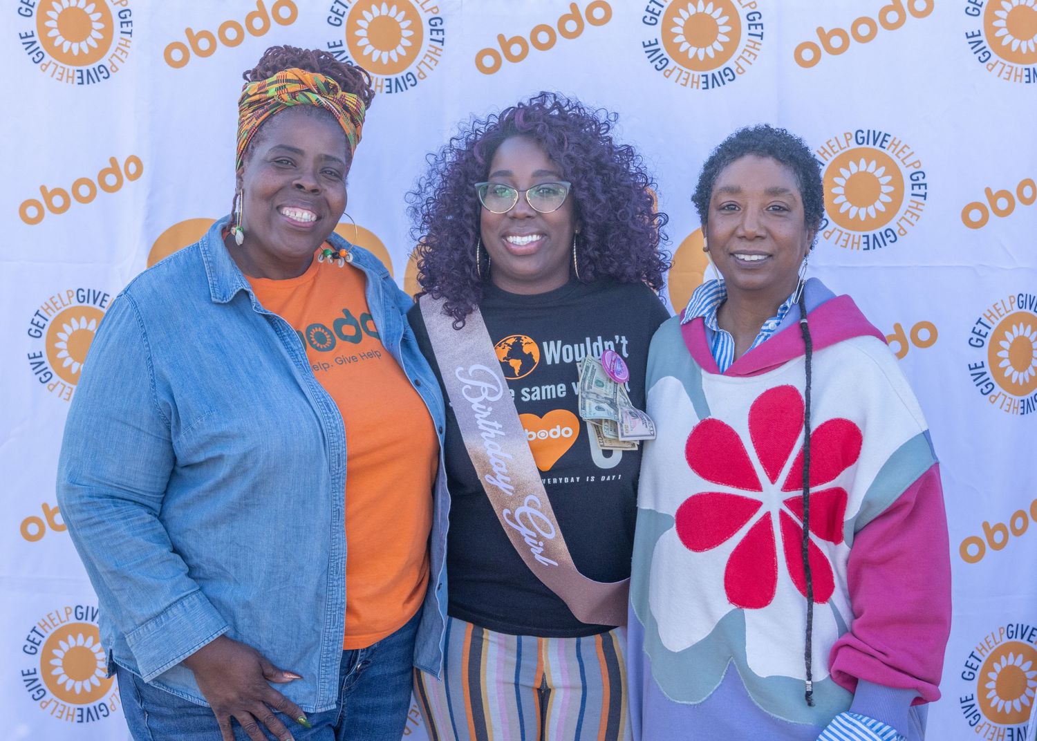 People celebrate at an event with repeating orange circular logo patterns on the backdrop wall.