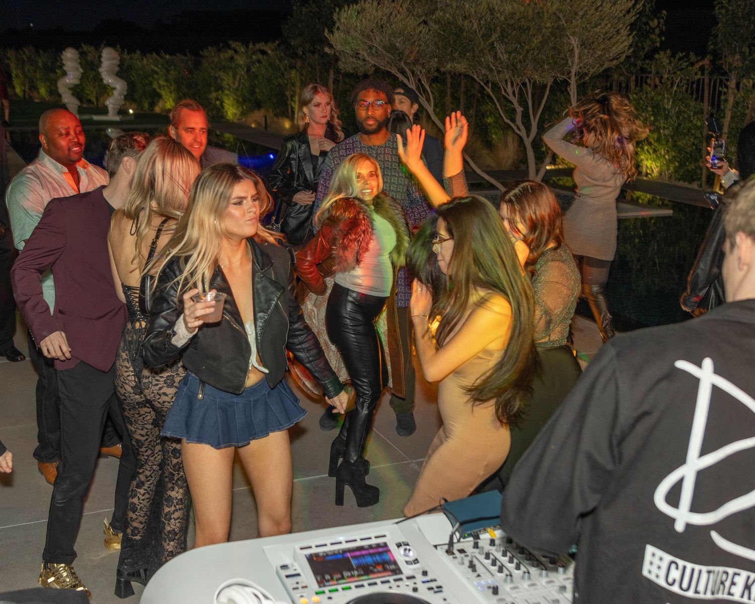 Nighttime party scene with people dancing and socializing outdoors.