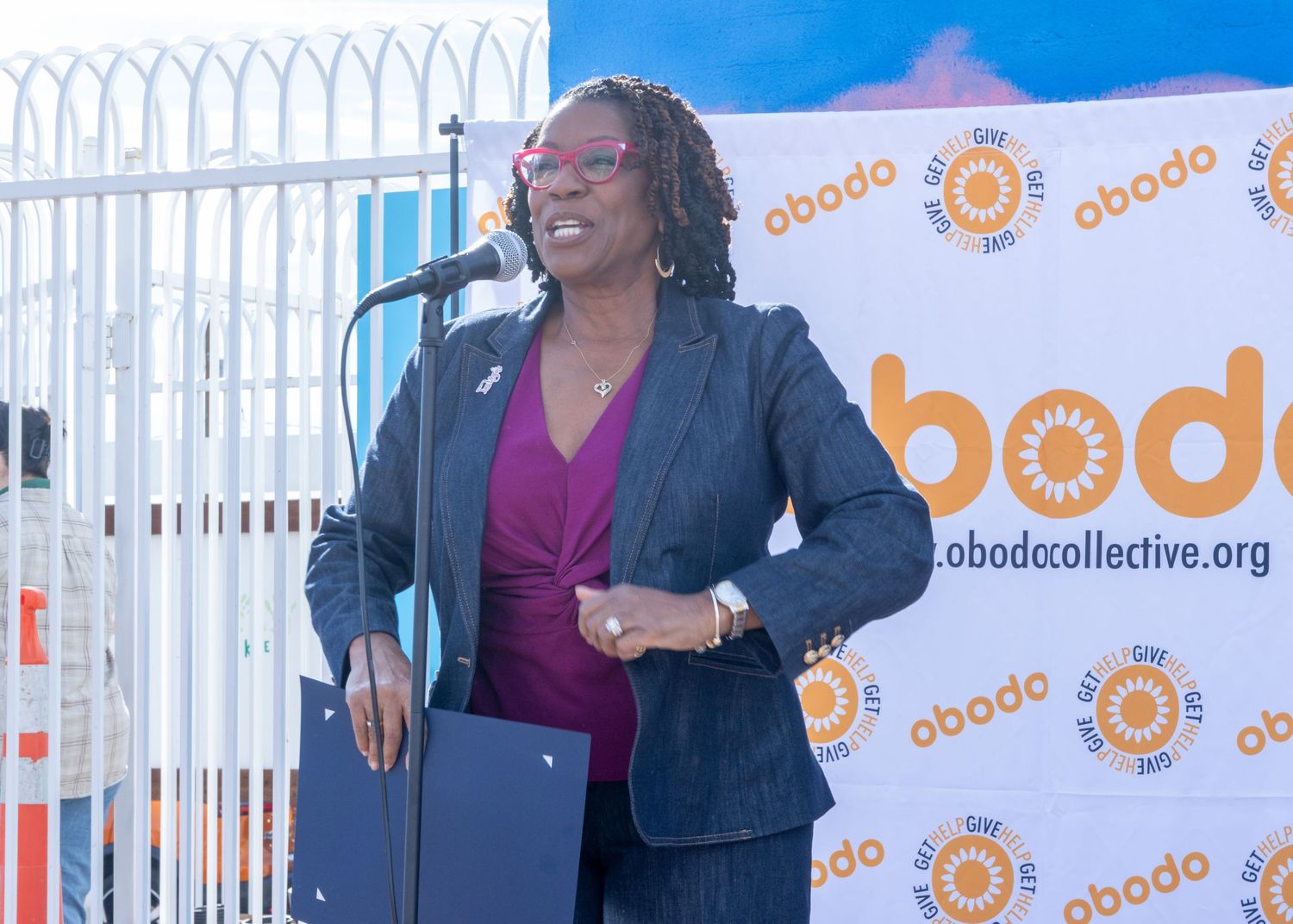 Three speakers present on stage with a bright orange and white branded backdrop at a business event.