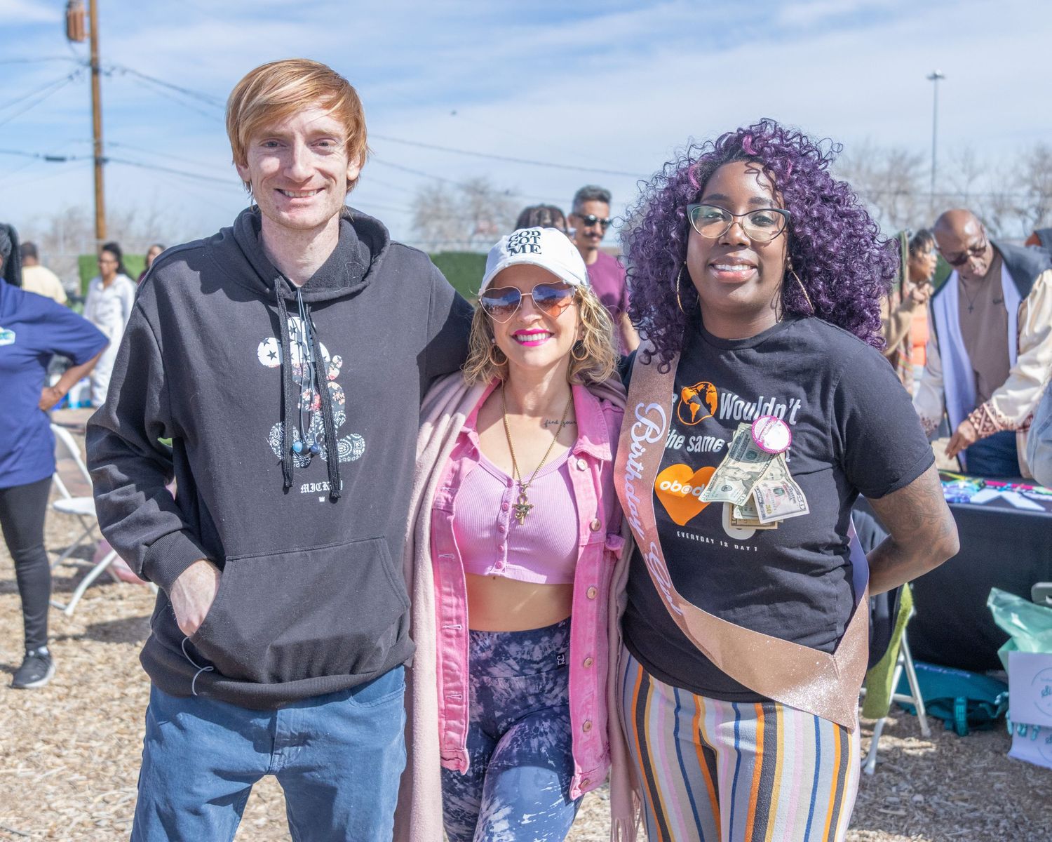 A group of people gather outdoors at a community event wearing casual attire on a sunny day.