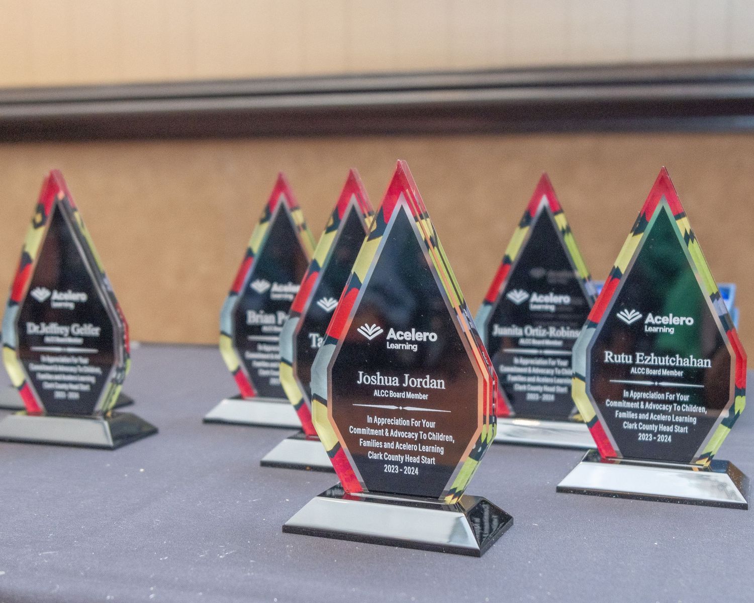 Row of crystal flame-shaped awards displayed on surface with colorful trim.