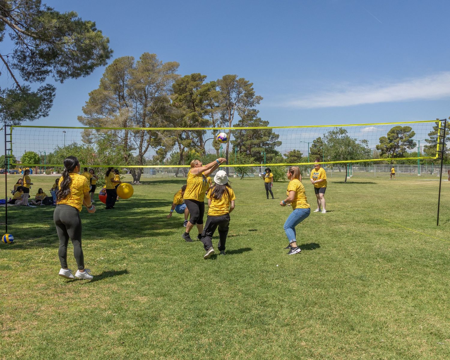 Wide view of yellow-shirted participants scattered across a grassy field during outdoor games.