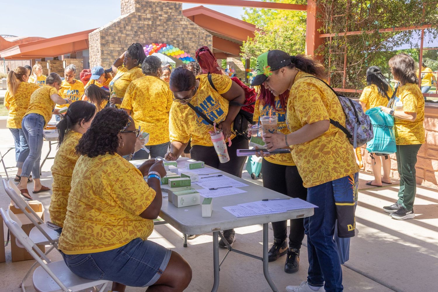 Group of people in yellow uniforms working at outdoor tables during a community gathering.