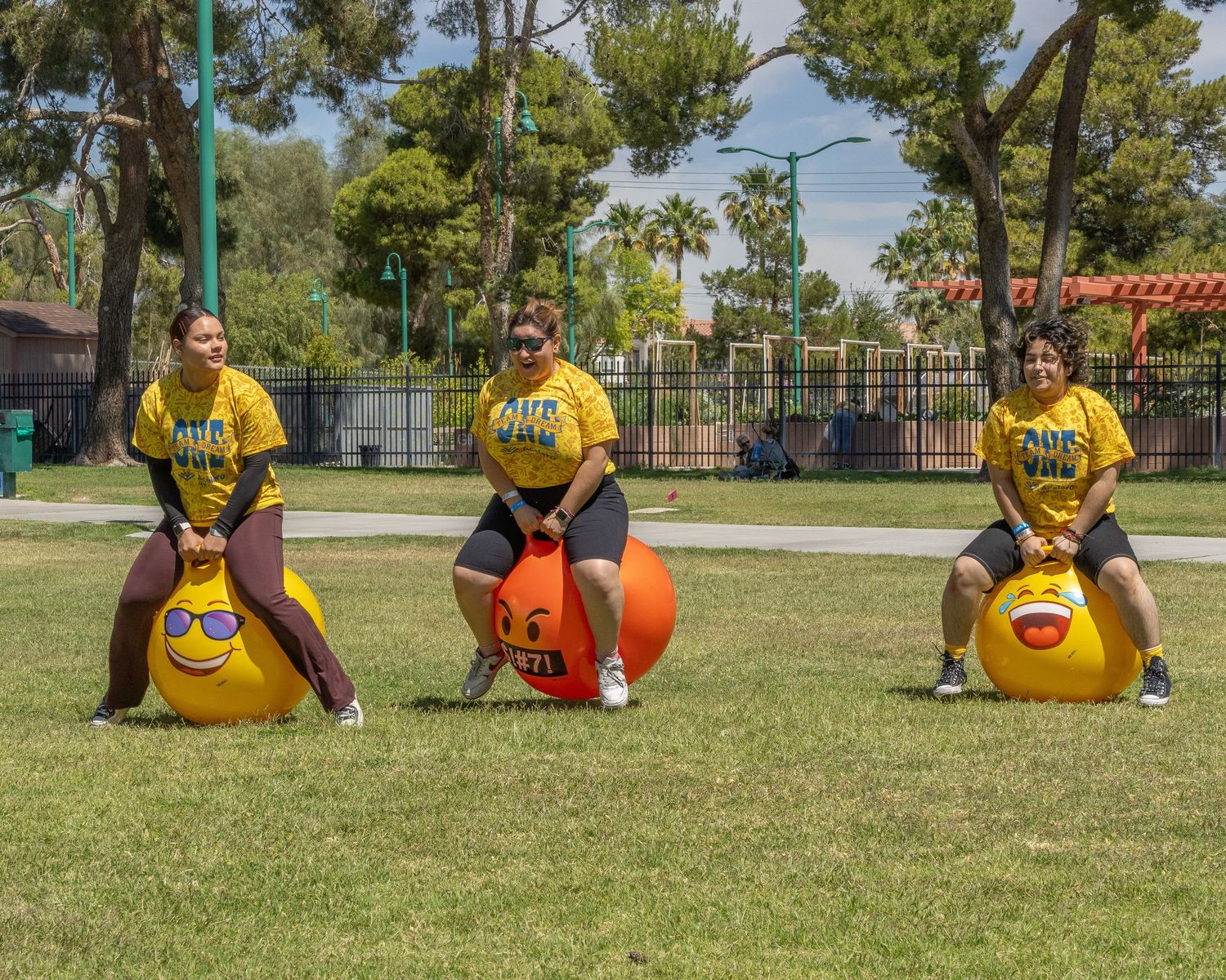 Group playing outdoor team building activities using large orange exercise balls on a sunny day.