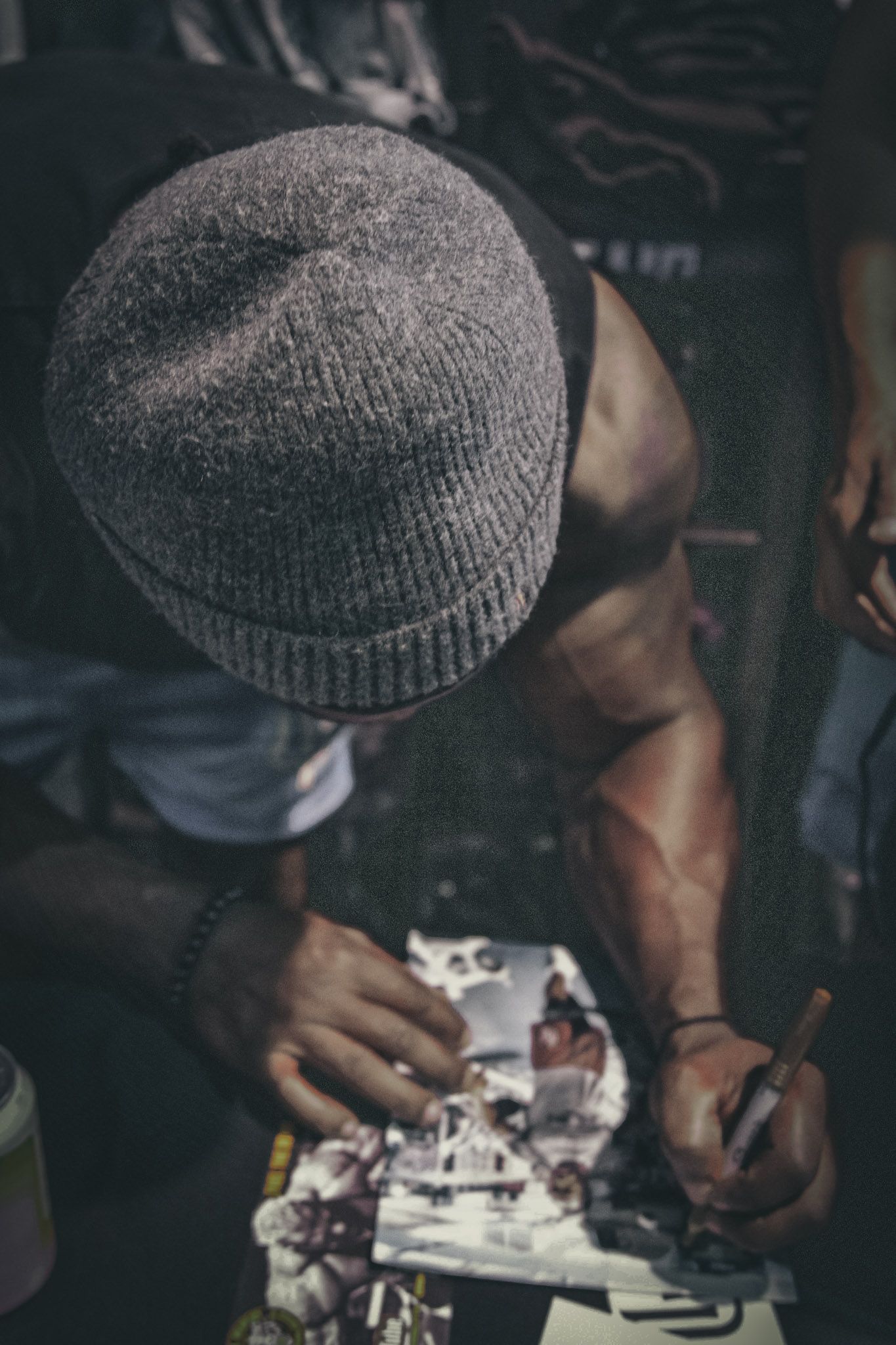 Person in knit beanie cap examining a gaming controller with close attention to detail in dimly lit setting.