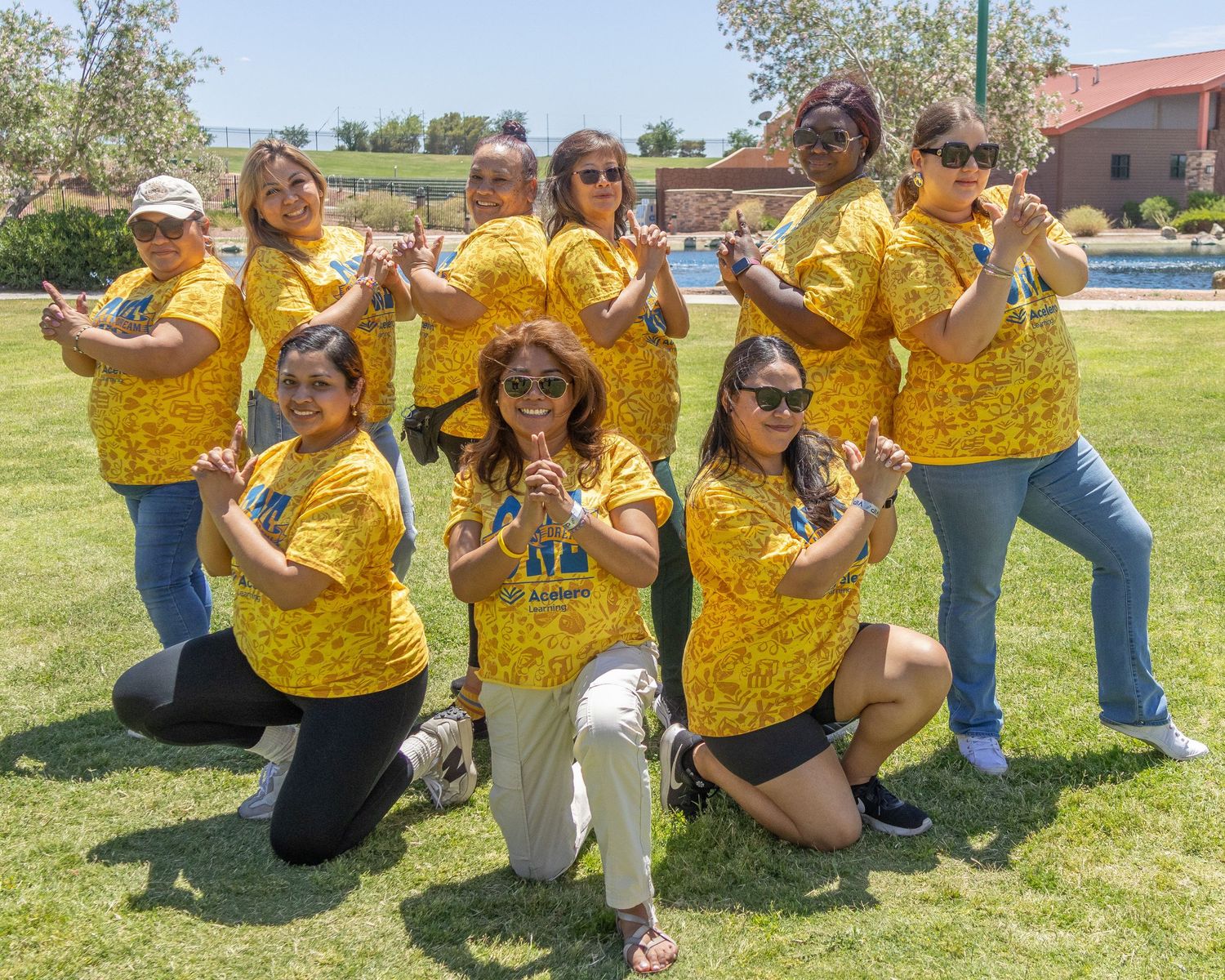 People in yellow shirts sitting casually on grass for outdoor group photo.