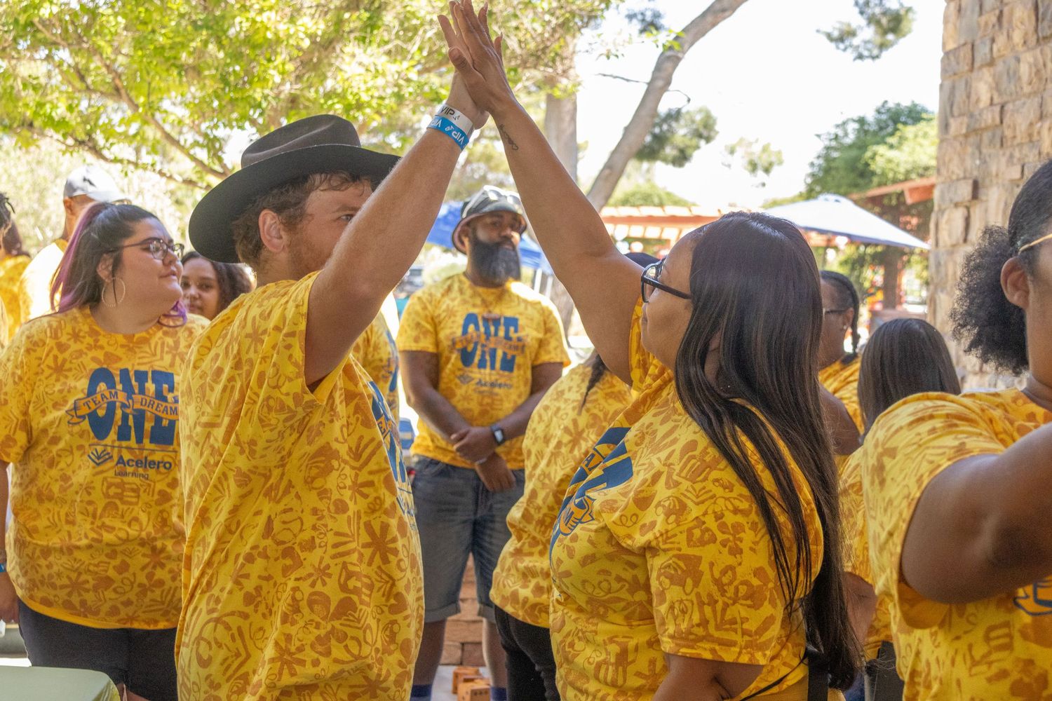 Crowd of people wearing yellow patterned t-shirts gathered at outdoor community event.