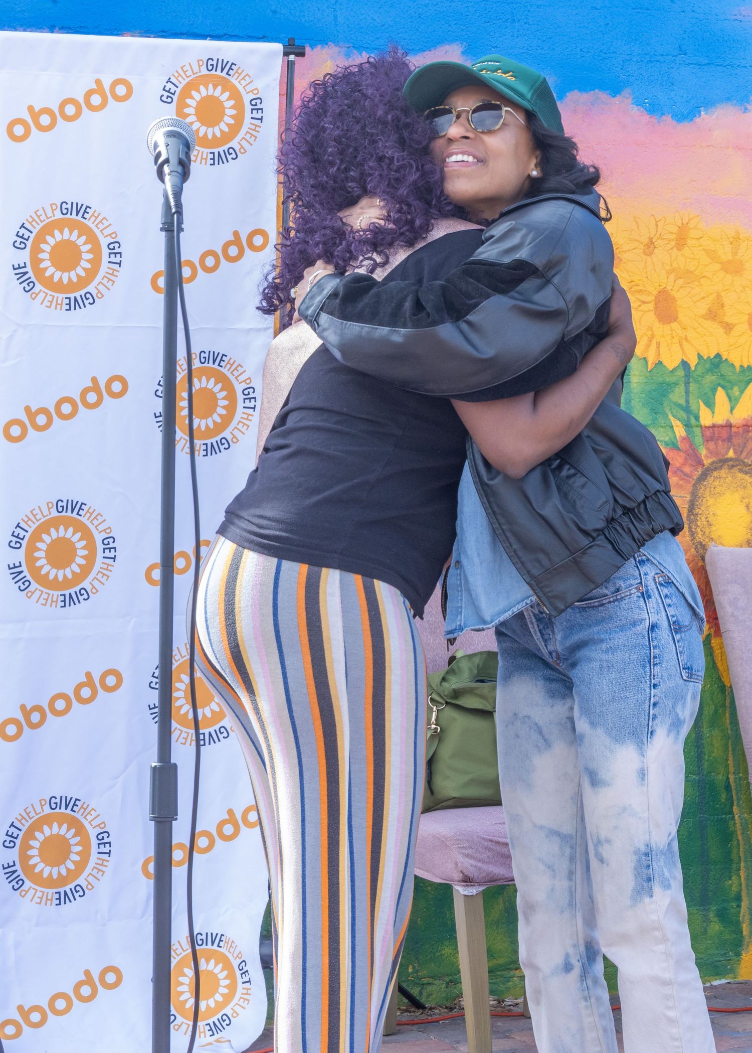 Two people share a warm embrace in front of a colorful backdrop with a sunflower design and Obodo branding.