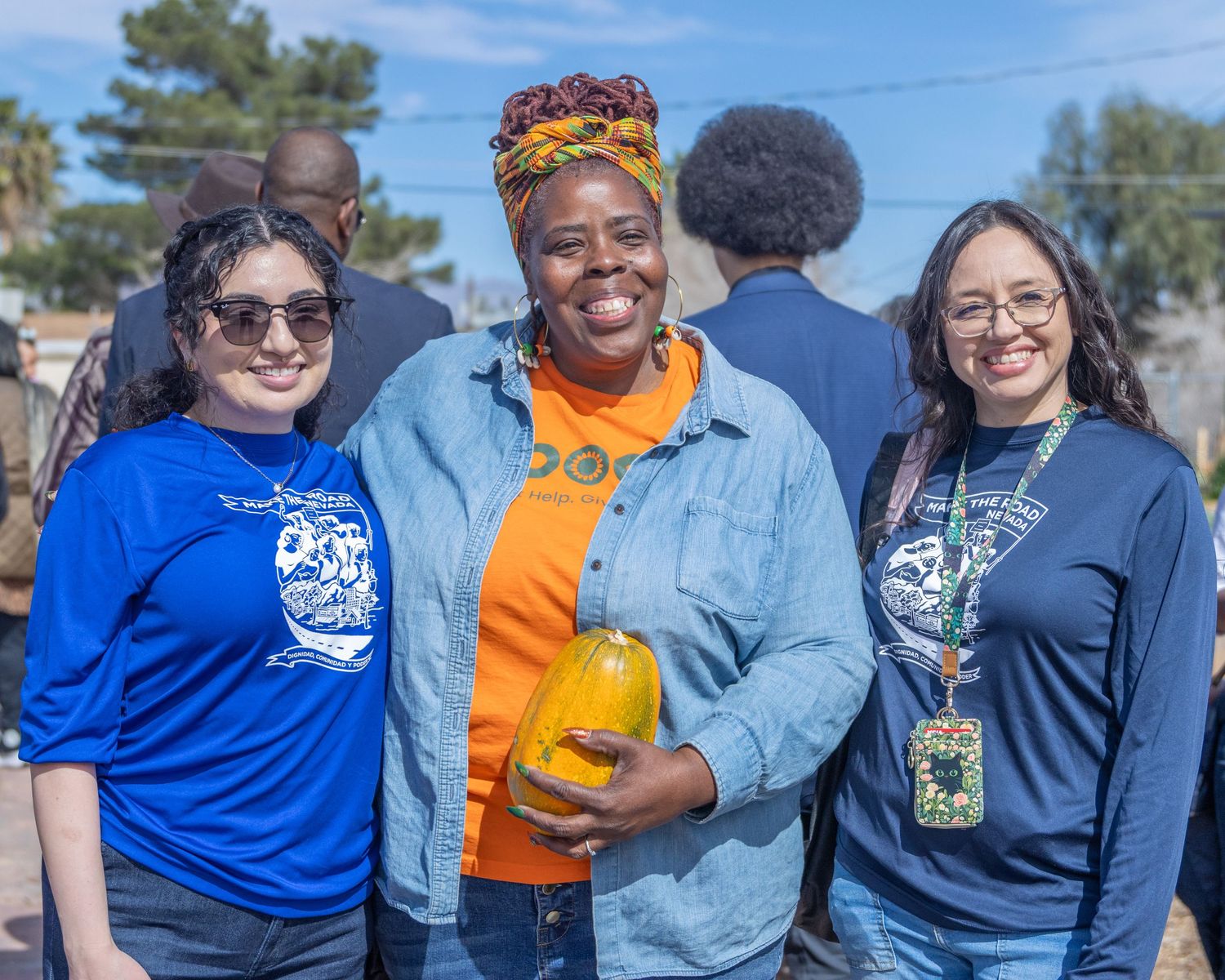 People wearing blue and orange shirts standing together at an outdoor event with palm trees in the background.