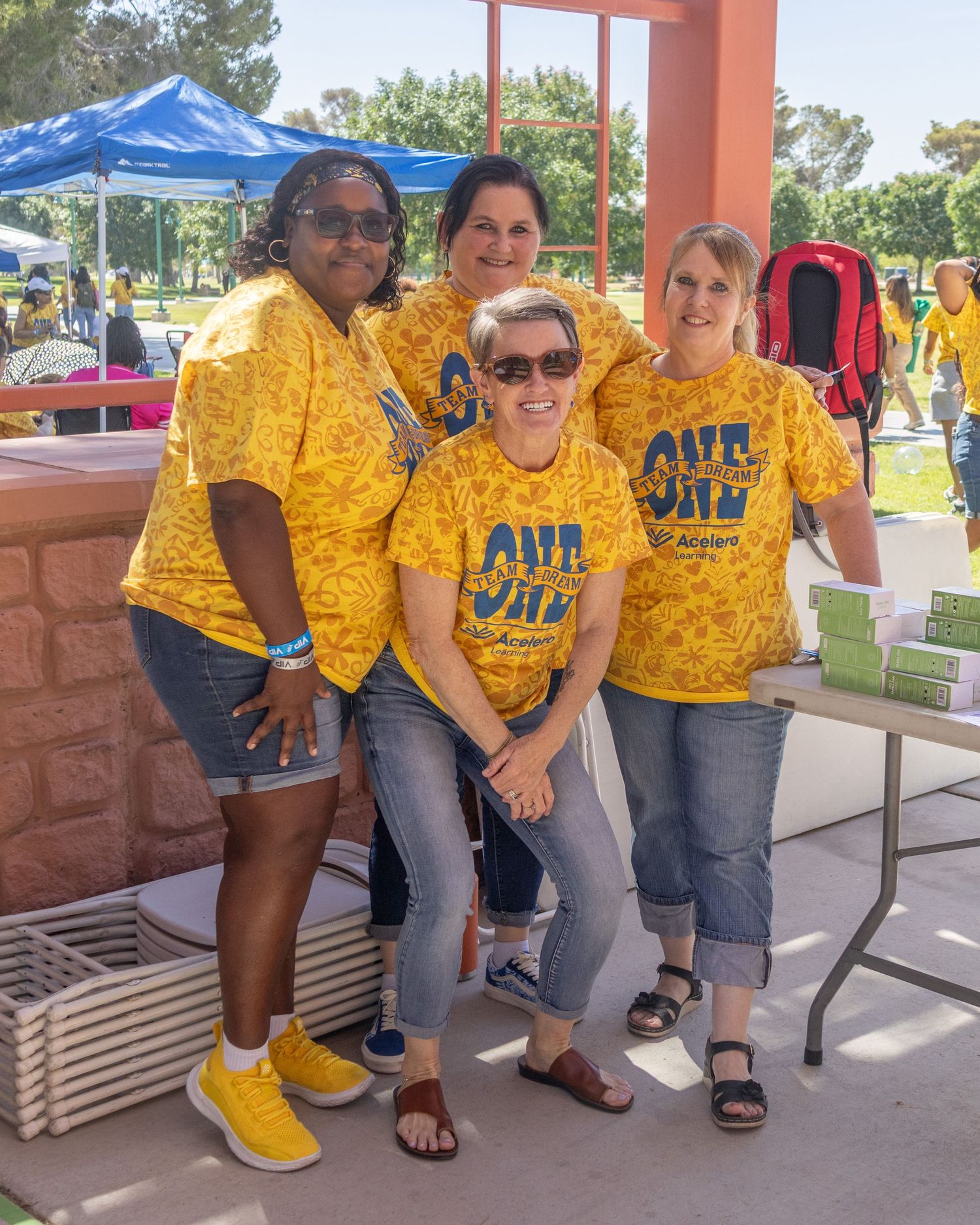 Group wearing matching yellow uniforms sits on bench outdoors during sunny day.