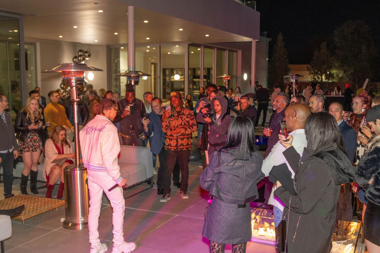 People gathering at outdoor event venue with pink ambient lighting and social atmosphere.