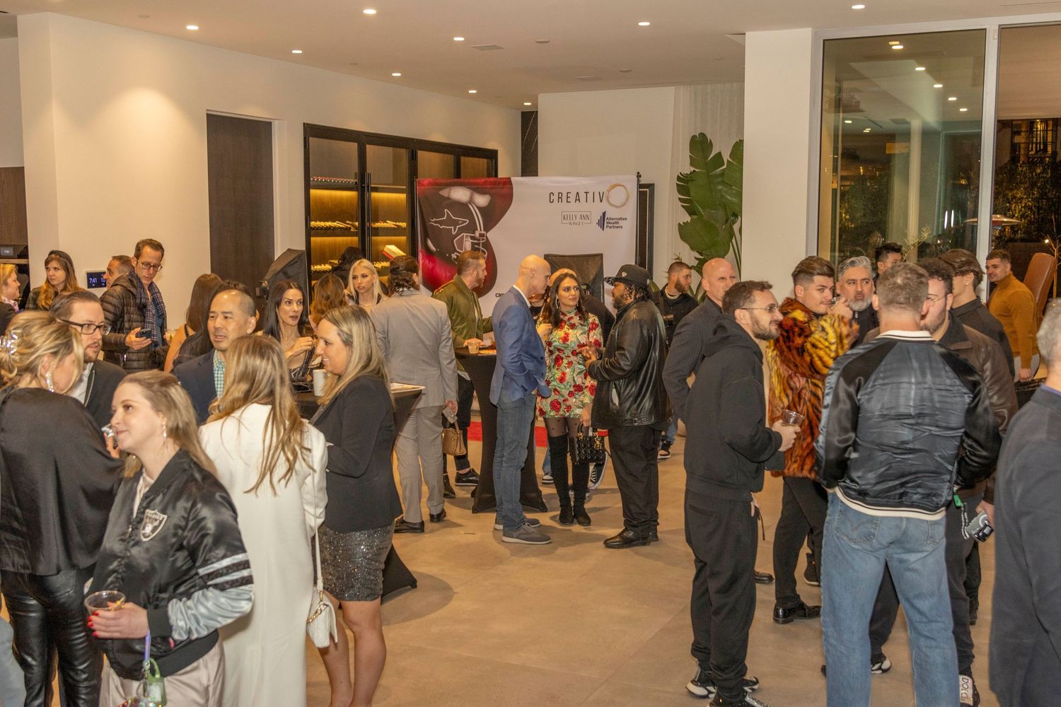 Wide shot of a crowded indoor event space with multiple groups of attendees socializing.