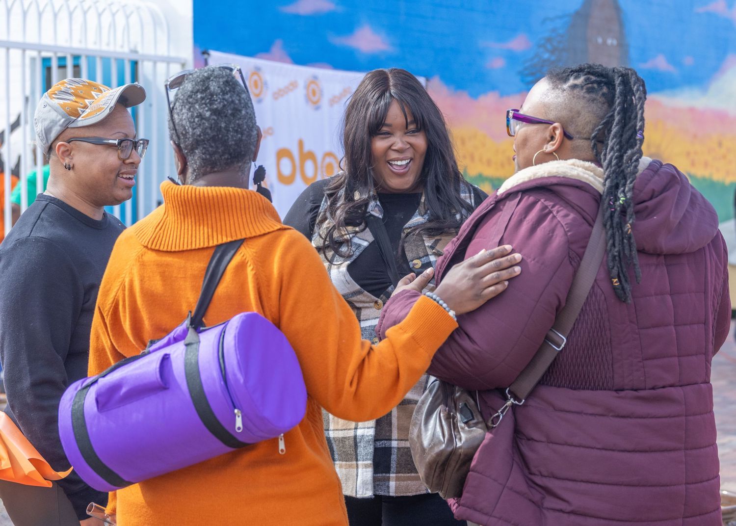 Diverse crowd in orange and purple sweaters gathered for a celebration event outdoors on a sunny day.
