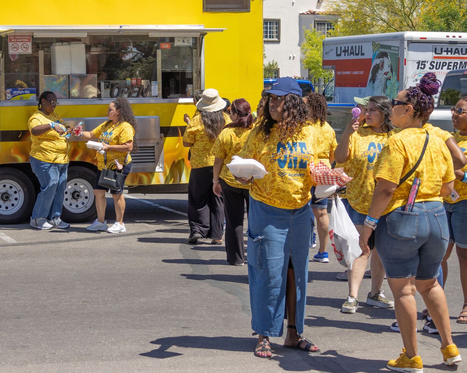 Group of people in yellow shirts gather outdoors by parked vehicles during a community event.