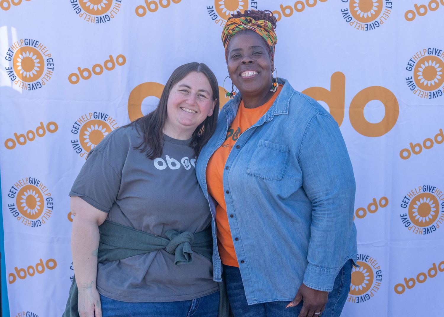 A group posing together at an outdoor event with orange and white circular logos on the wall behind them.