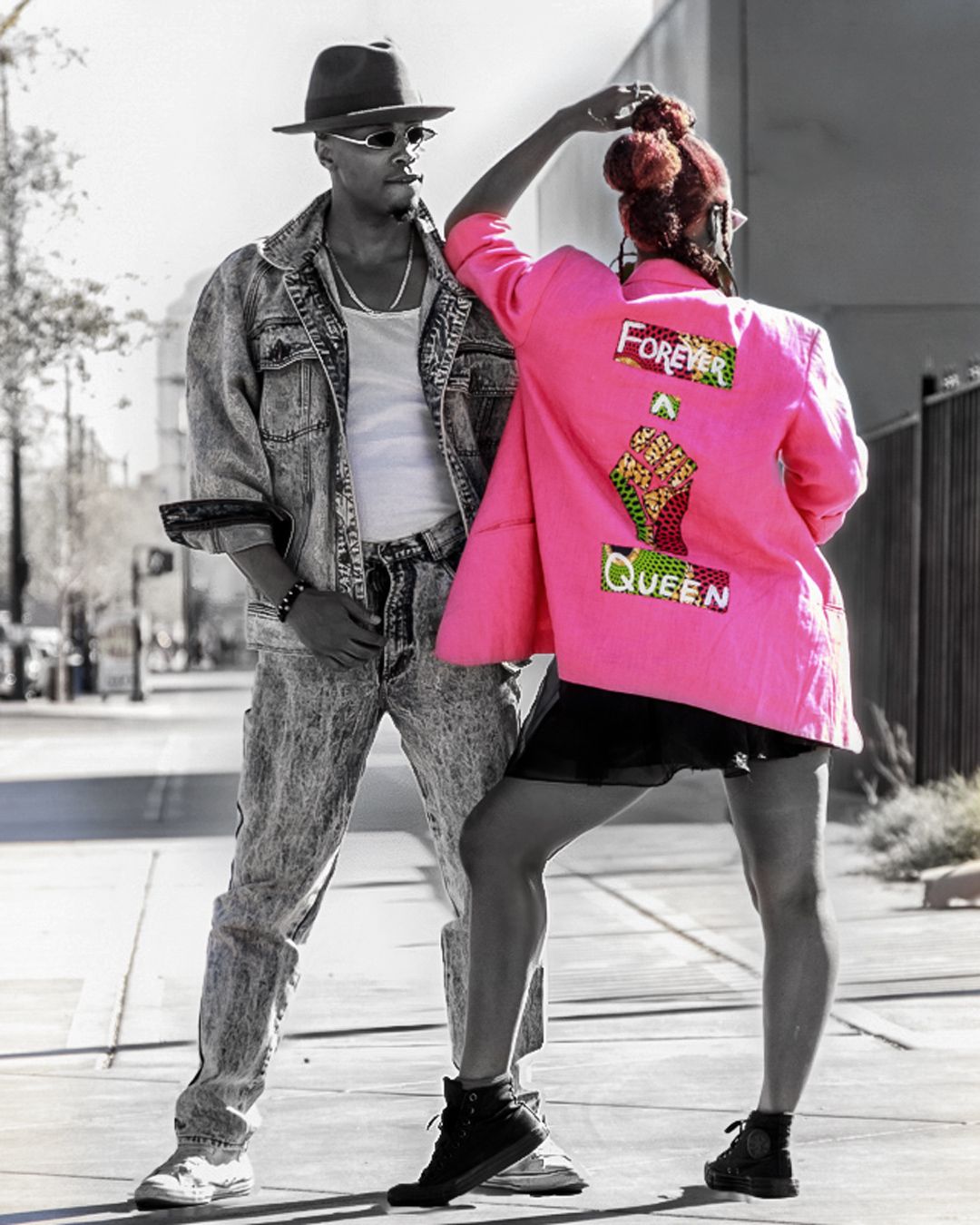 A person wearing jeans and a bright pink varsity jacket poses against an urban black and white background.