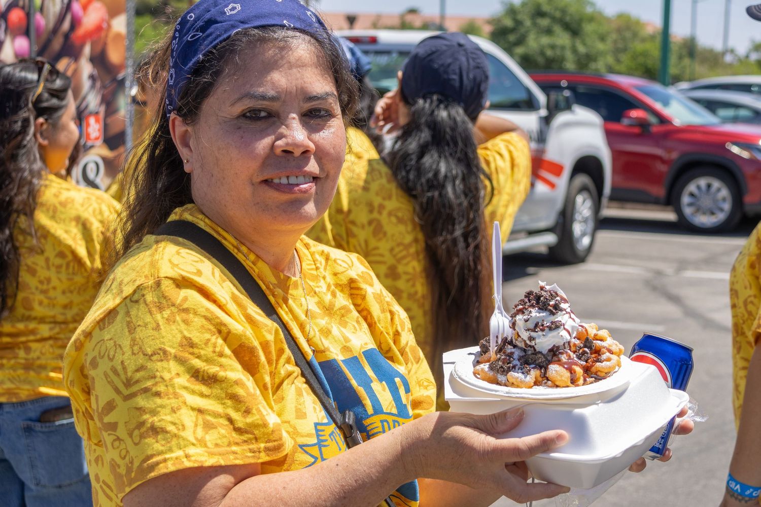 People gather at an outdoor food event enjoying dishes while dressed in colorful traditional attire.
