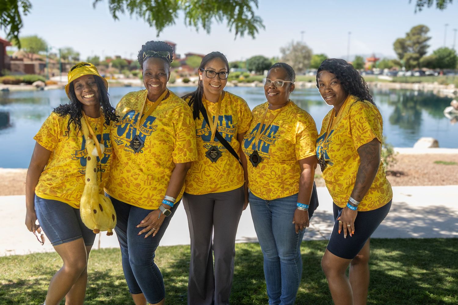 Group photo of team members in matching yellow shirts posing by lakeside setting.
