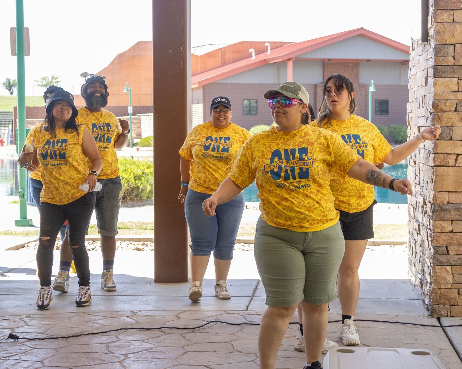 Group in yellow team shirts dancing together under a covered outdoor area during an event.