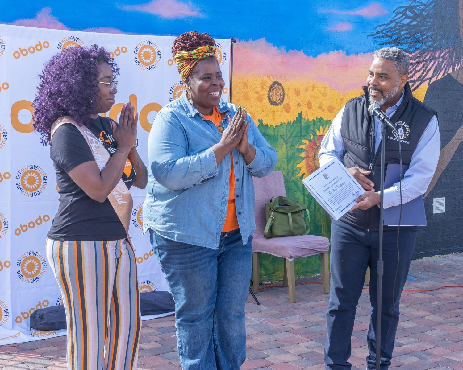 Group of people standing together and interacting at an outdoor networking event with colorful mural backdrop.