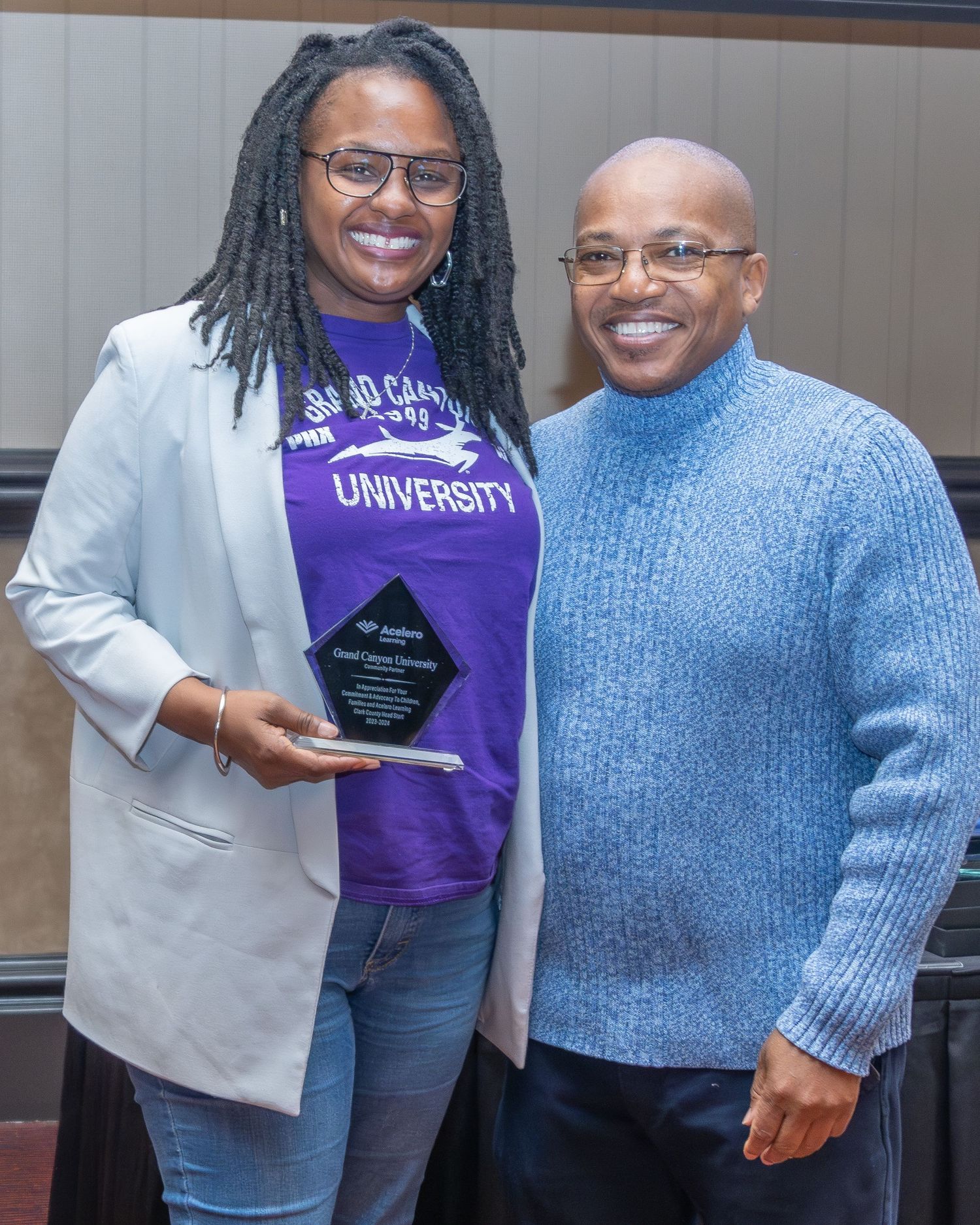 People in casual attire gather around a person wearing a purple university shirt holding an award.