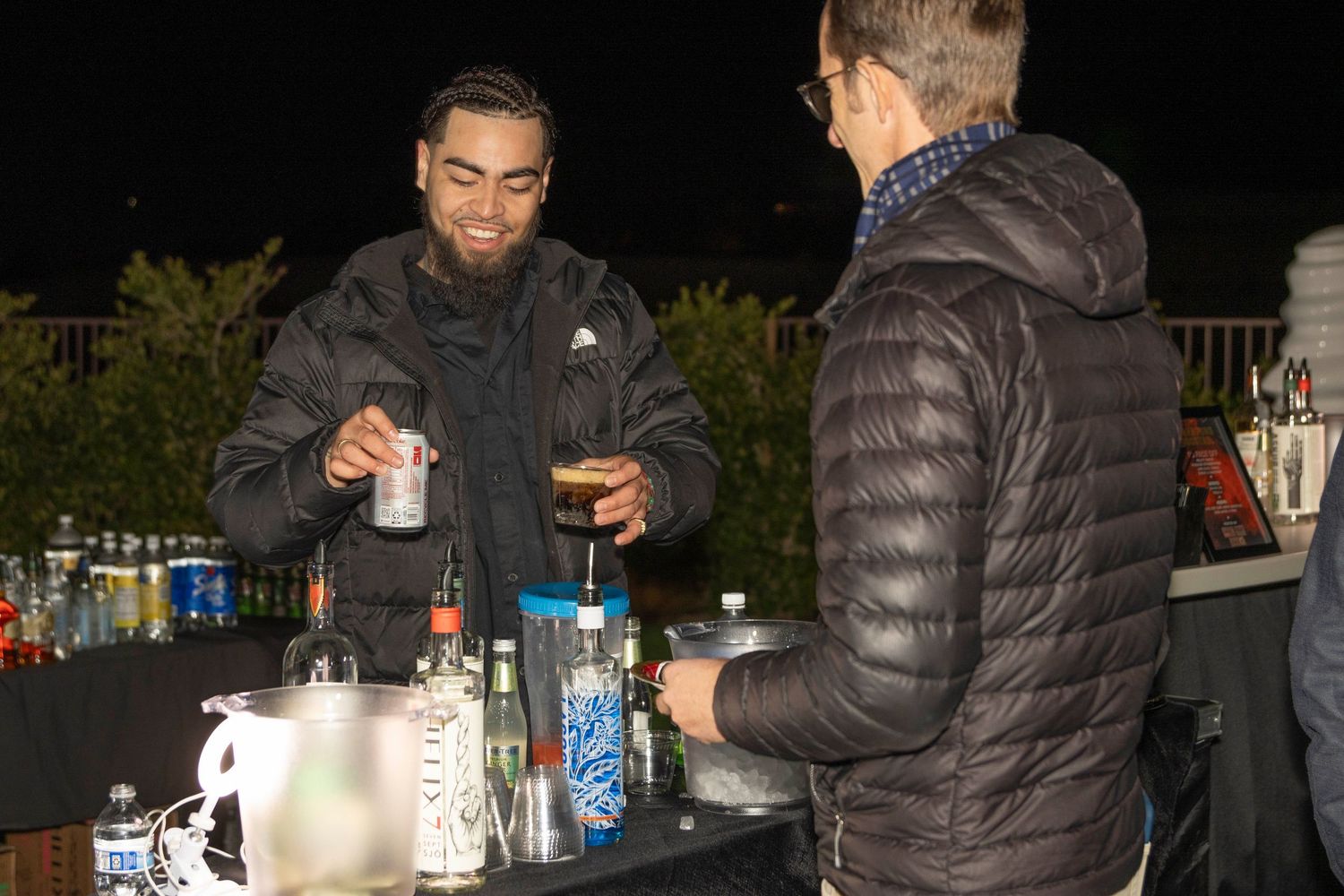 People gathered around drinks at an outdoor nighttime social event.