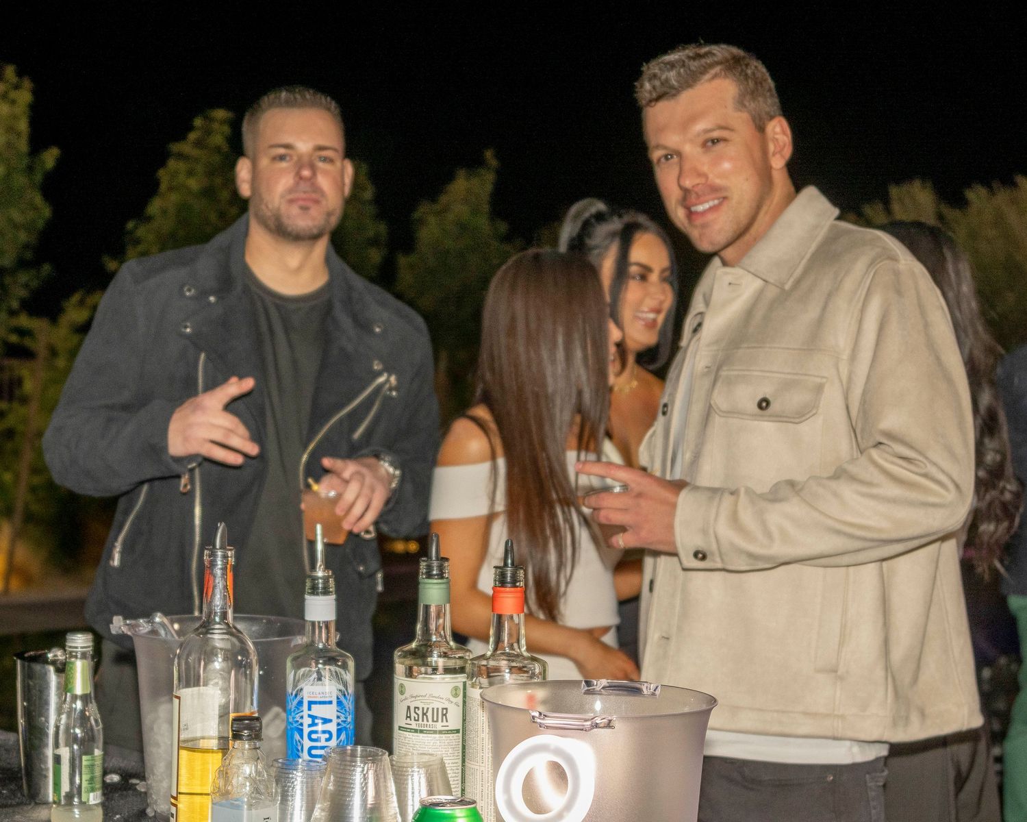 Group enjoying drinks and conversation at an outdoor table with bottles.