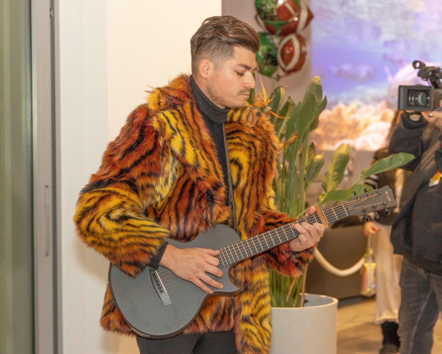 Performer in vibrant tiger print coat playing guitar near indoor plants.