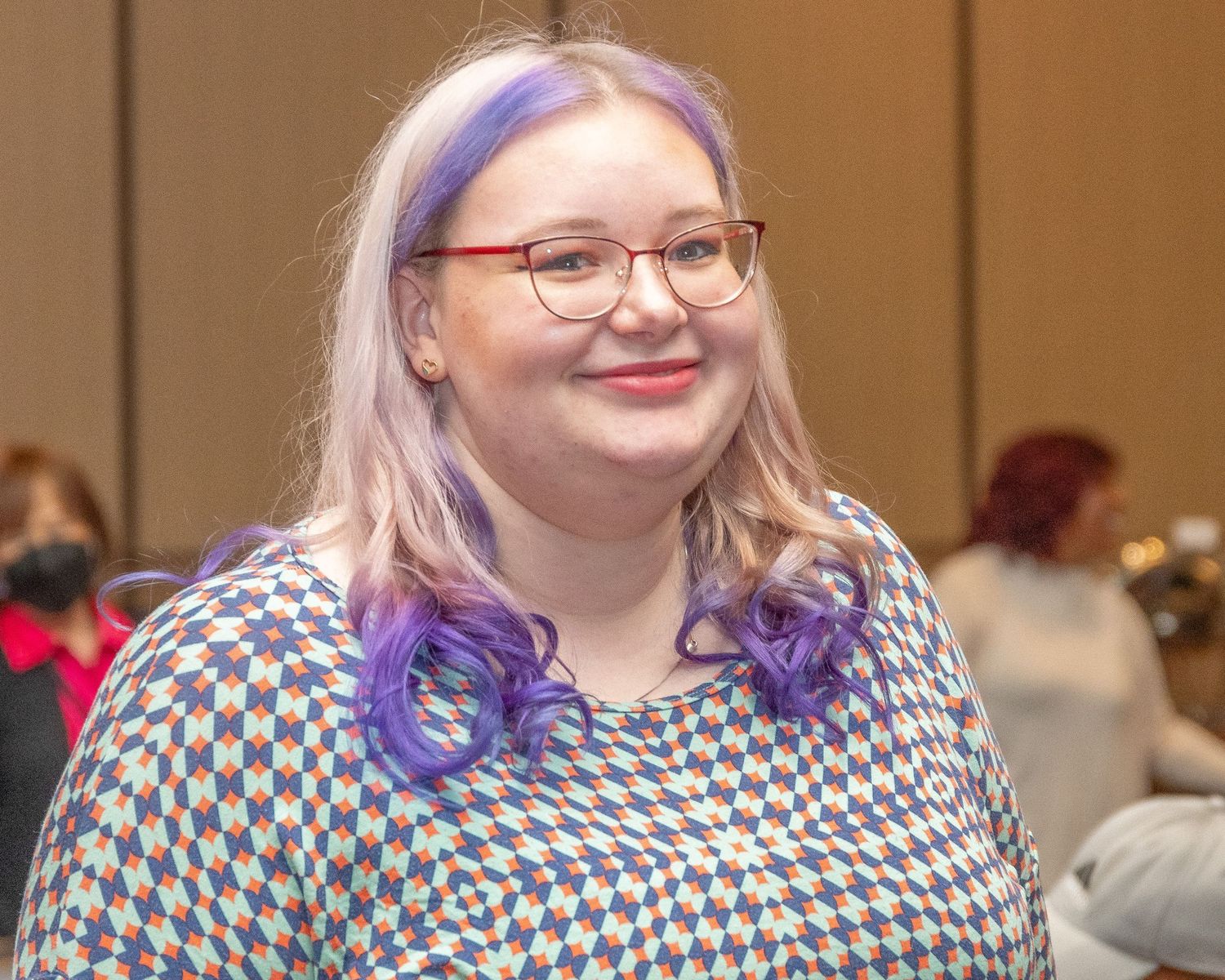 Person in checkered pattern top smiling during indoor gathering.