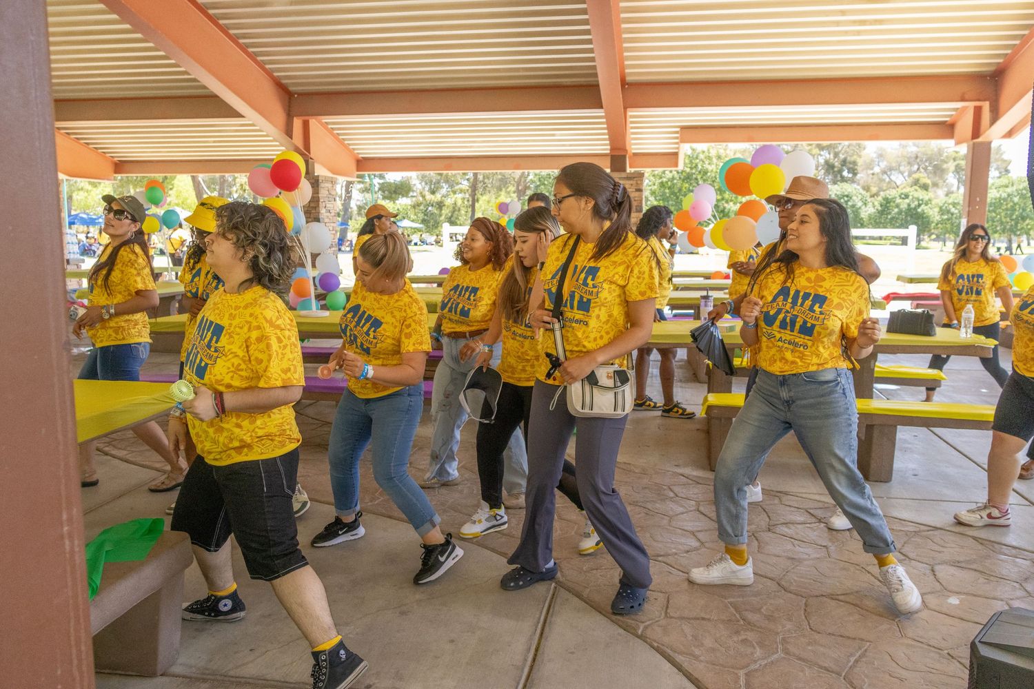 Energetic group dance routine performed by team members wearing matching yellow shirts outdoors.