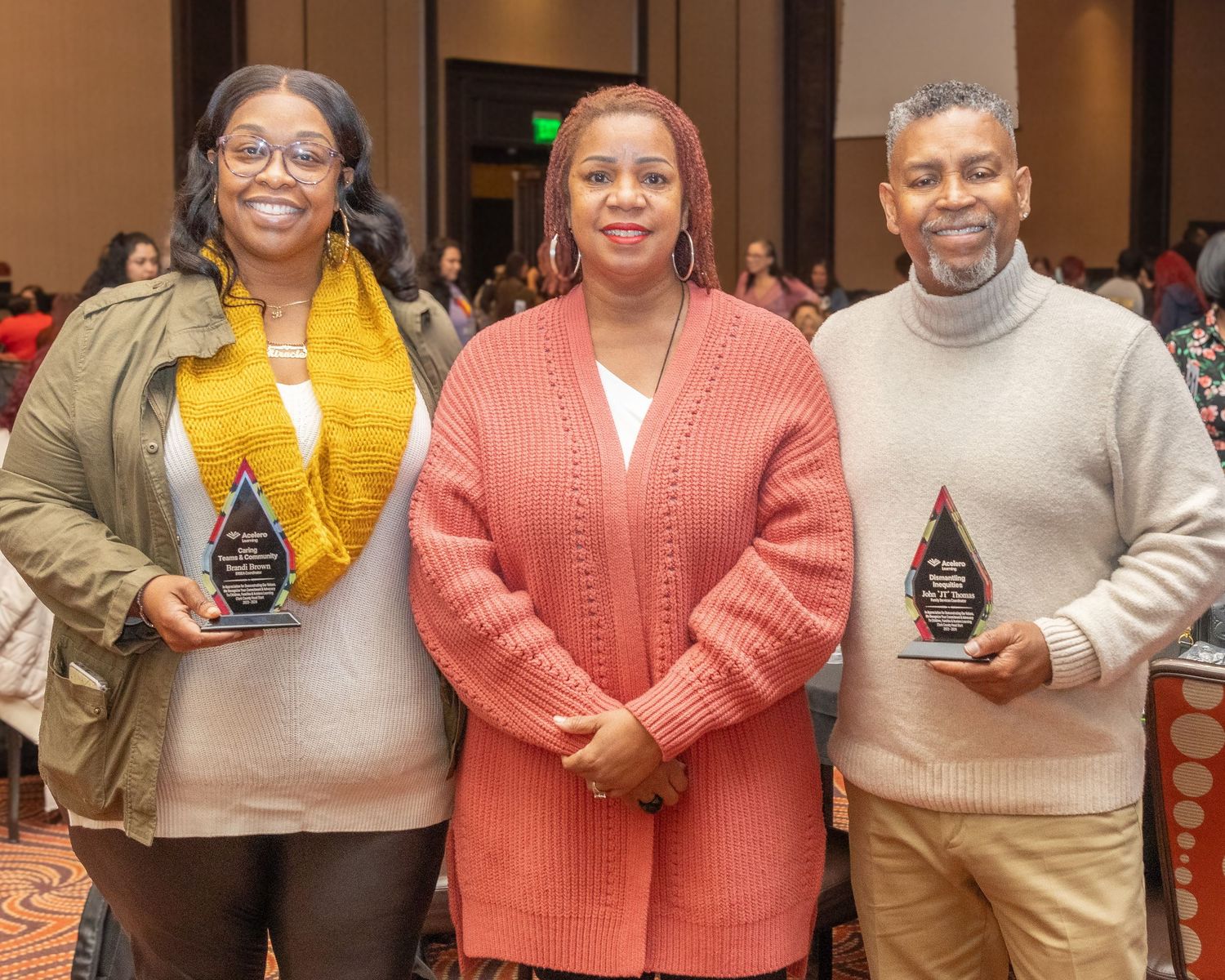 Three award recipients pose with crystal trophies wearing colorful sweaters.