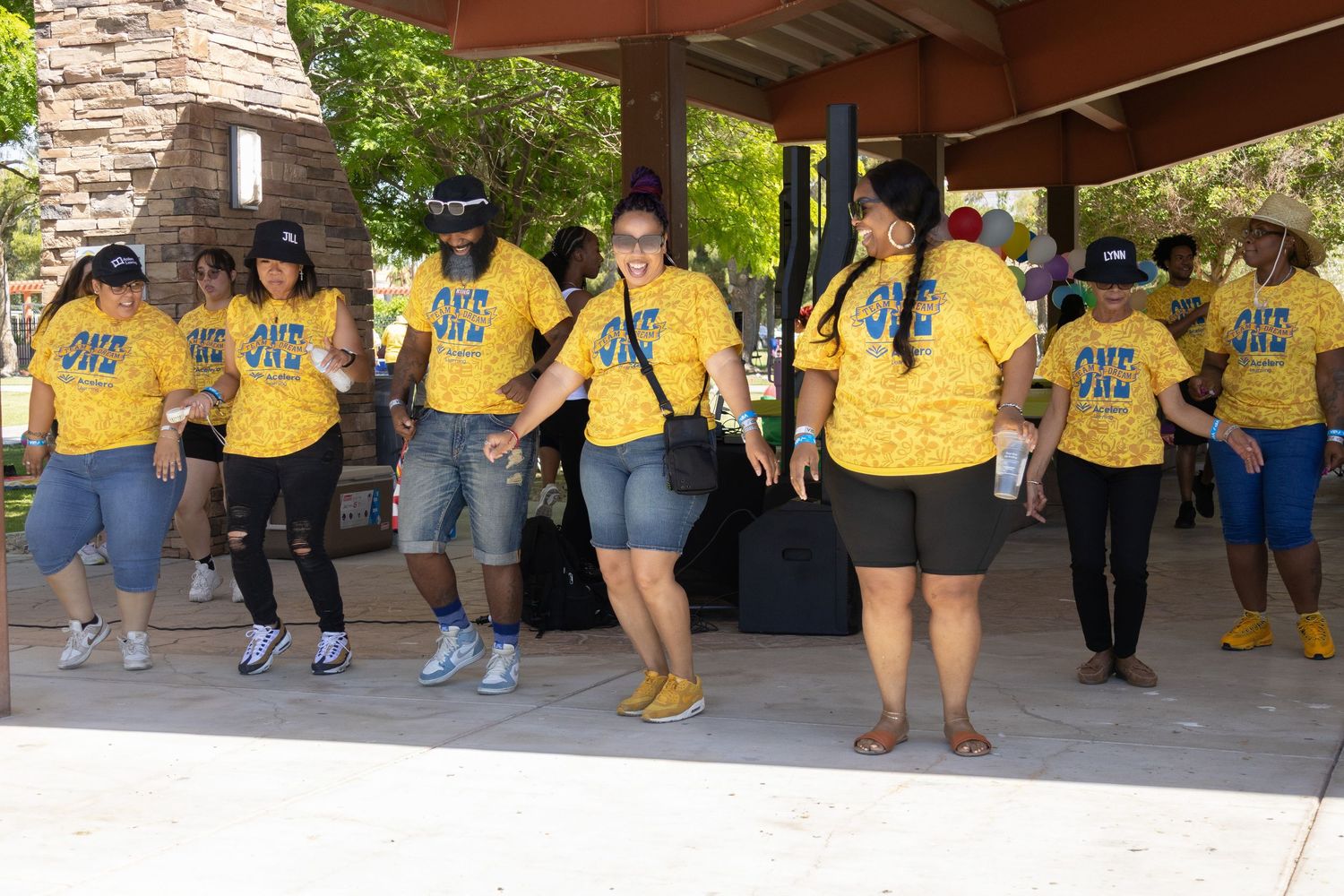 People in matching yellow shirts gathered under covered pavilion during daytime event.