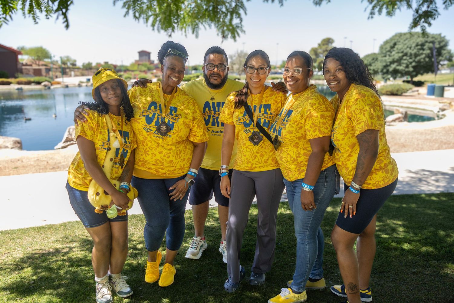 Group wearing matching bright yellow t-shirts posing together by a lakeside park.