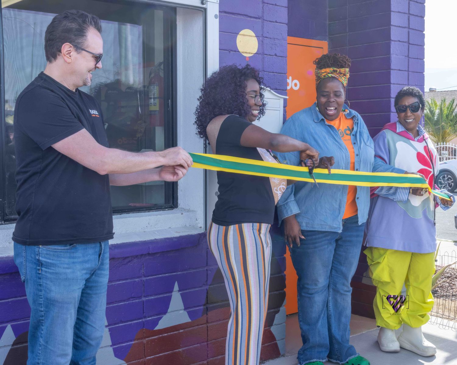 People participate in a ribbon cutting ceremony outside a building with purple walls.