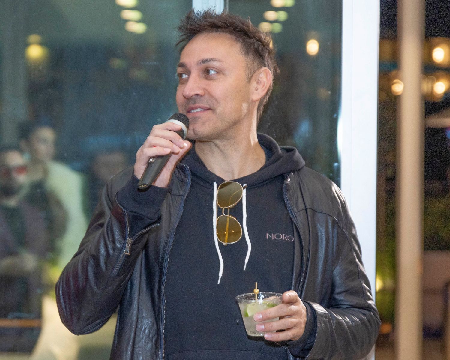 Person in dark hoodie holding a drink at indoor event.