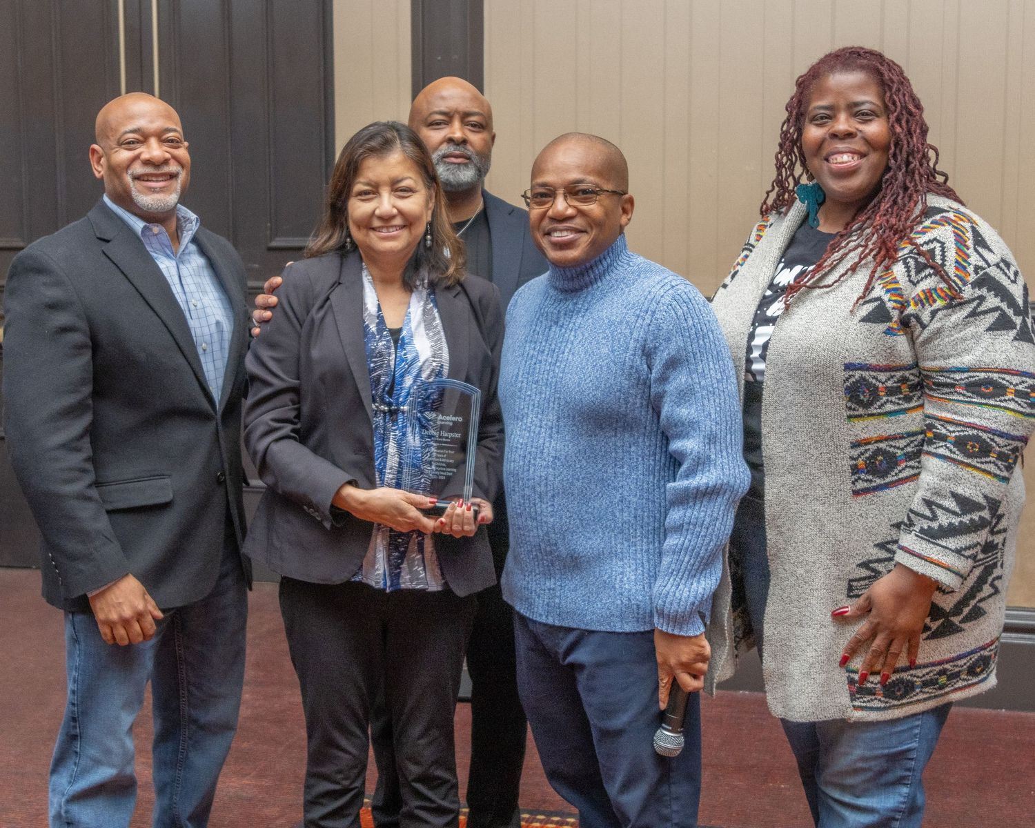 A group of people gather and smile while celebrating with an award at an indoor event. Tameka Henry