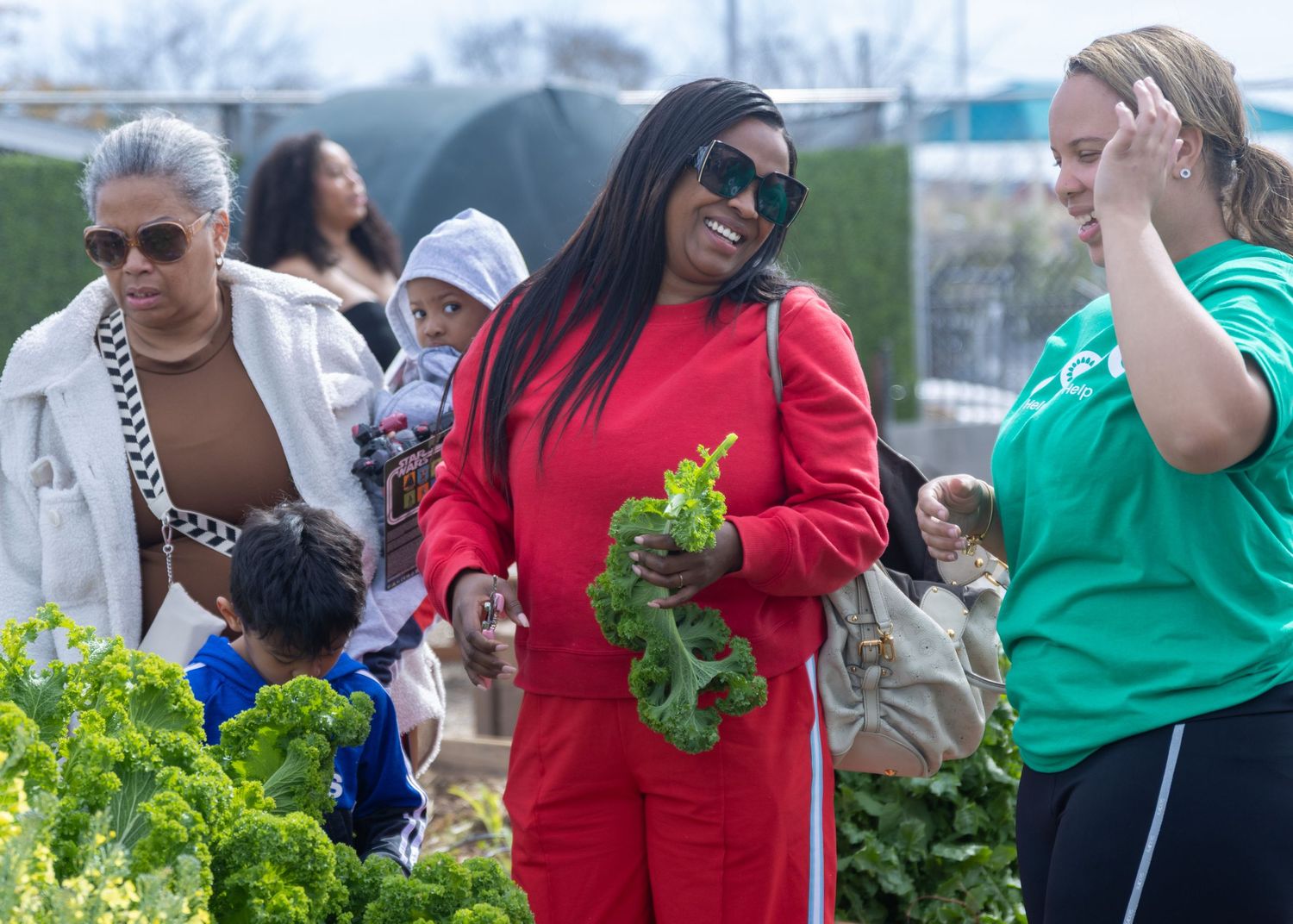Community members gather vegetables and produce at an urban garden harvest event.
