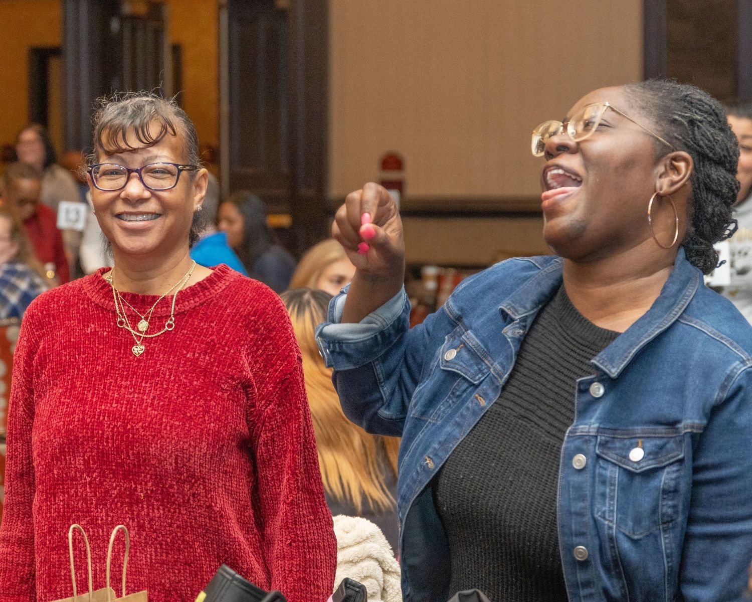 Two attendees share a lively moment of laughter at indoor gathering.