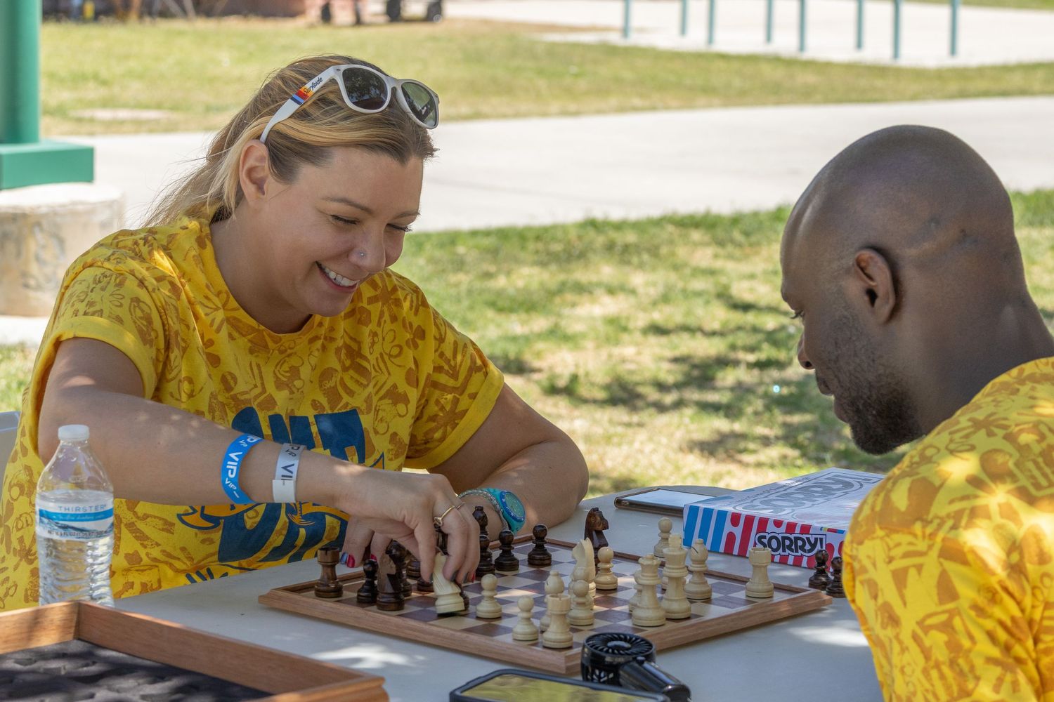People in yellow t-shirts engaged in chess matches and games during an outdoor event.